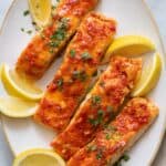 Large oval serving dish with 4 harissa glazed salmons filets garnished with lemon wedges and parsley.