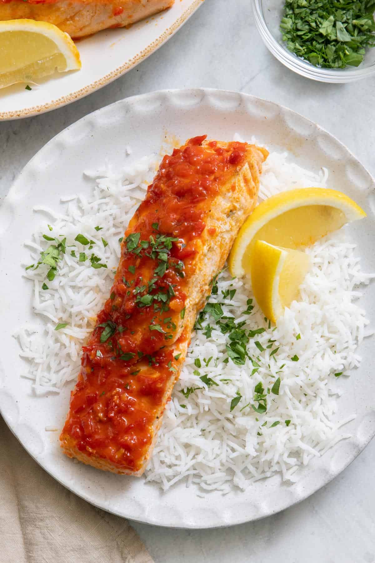 Plate of white rice, salmon, lemon wedges and chopped parsley.