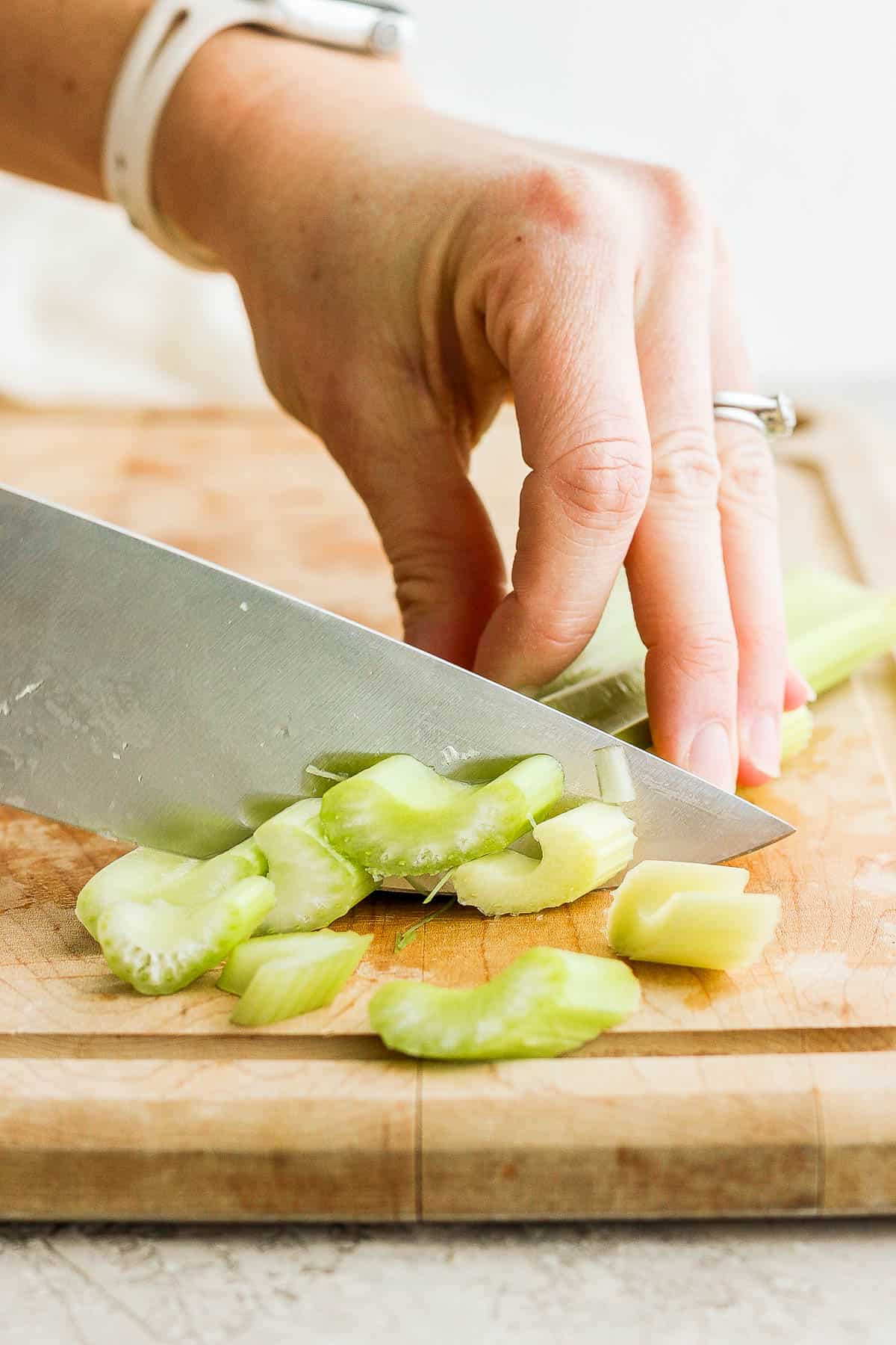 Celery on cutting board being cut on a bias.