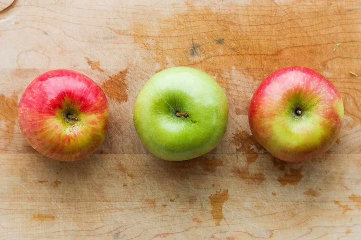 Top down view of 3 different colored apples on a cutting board.