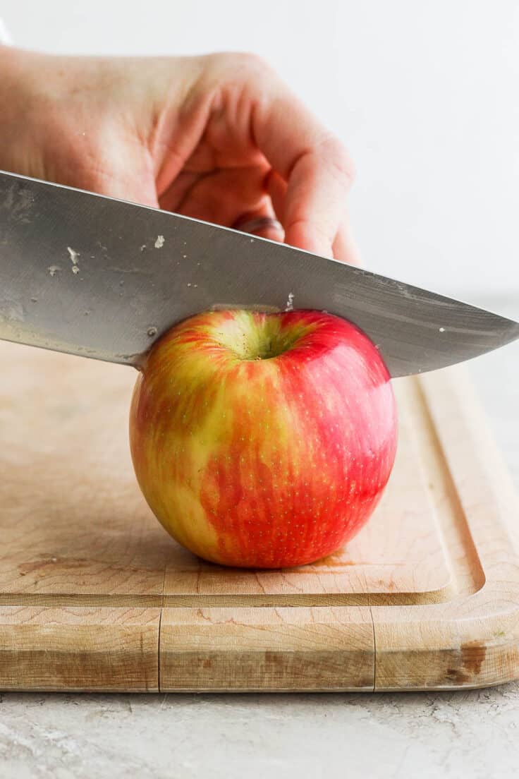 An apple being cut on a cutting board with a large knife.