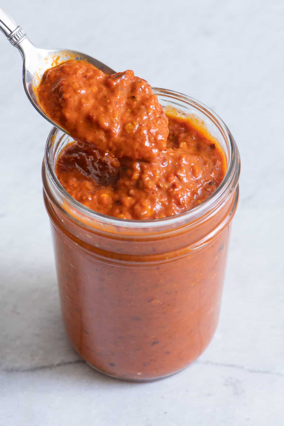 Harissa paste in glass jar with spoon scooping some up.