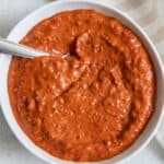 Harissa paste in white bowl with spoon dipped inside.