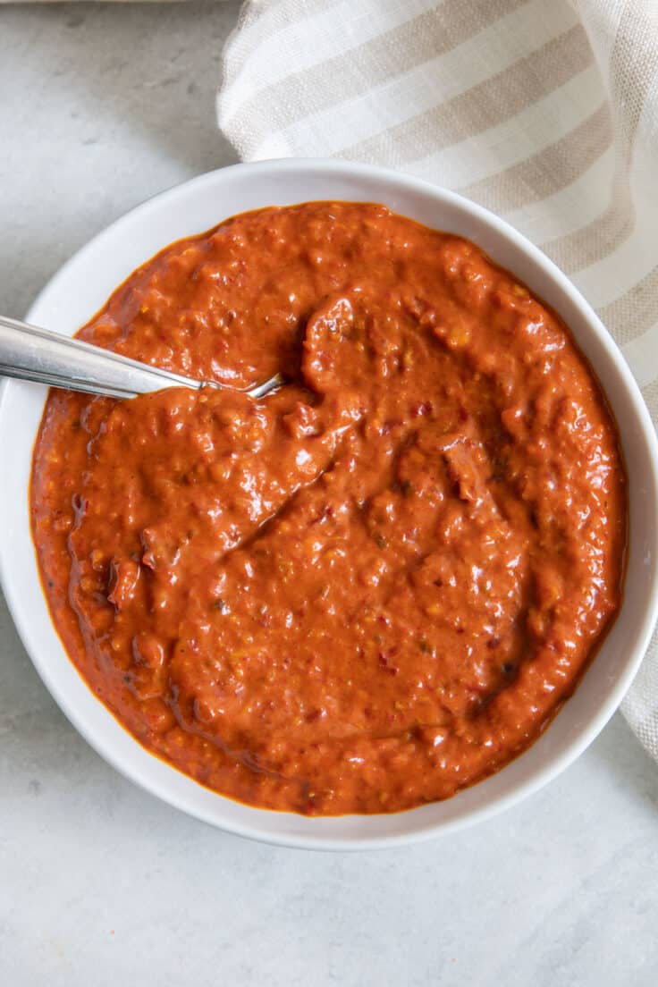 Harissa paste in white bowl with spoon dipped inside.