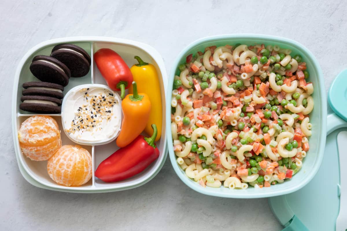Stackable lunch container with individual sections and different foods in each: 4 cookies, 2 peeled clementines, cream cheese with everything but bagel seasoning, mini bell peppers, and a large container with macaroni salad.