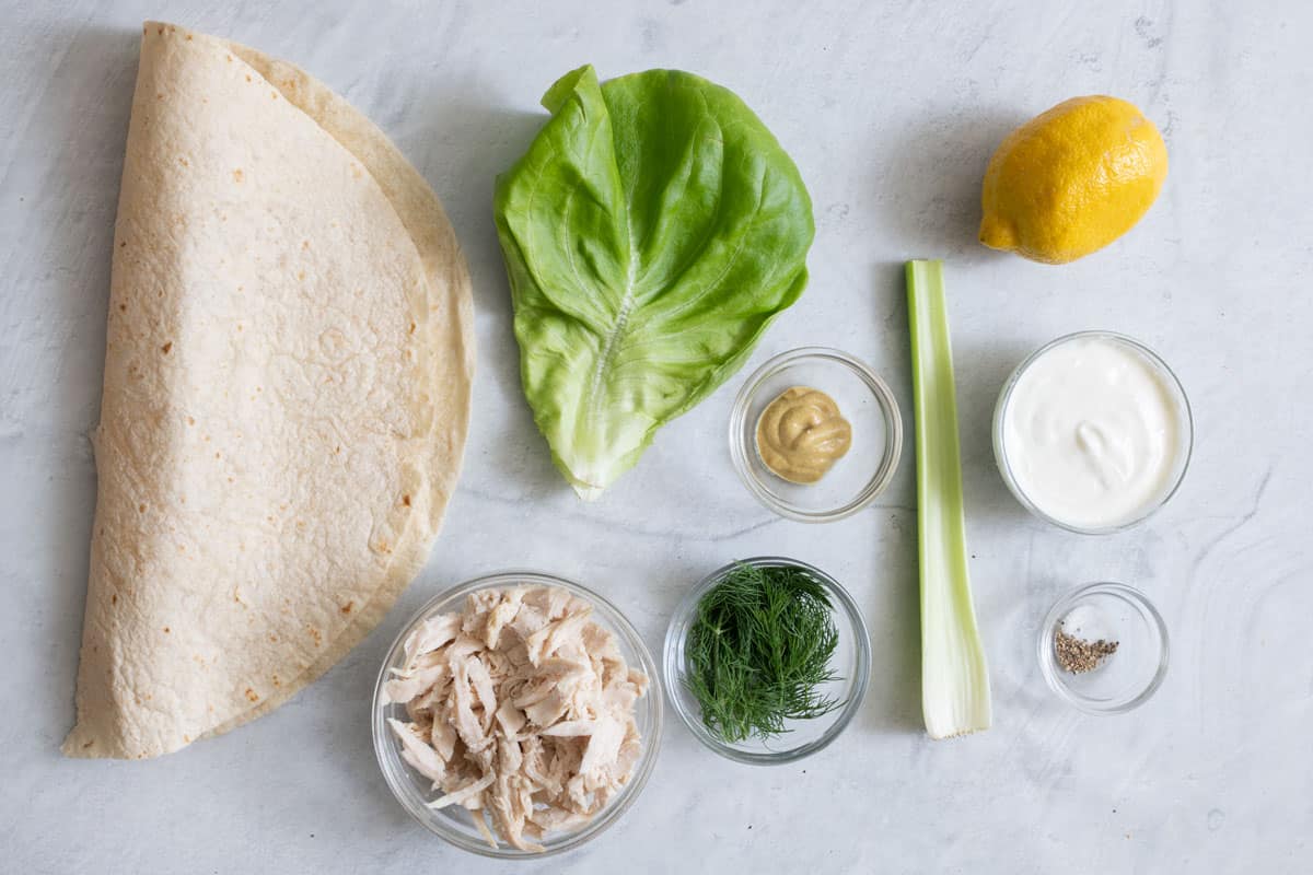 Ingredients for recipe: large tortilla shell, chopped chicken, leaf lettuce, dill, mustard, celery stalk, lemon, greek yogurt, and seasonings.