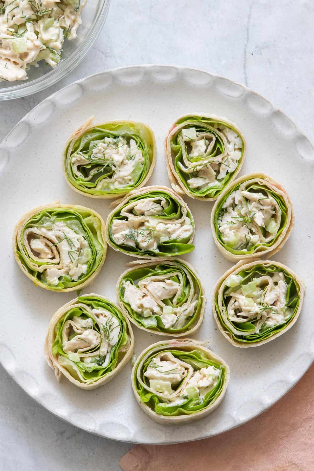 Chicken Salad pinwheel sandwiches on a round plate with ingredients off screen on sides.