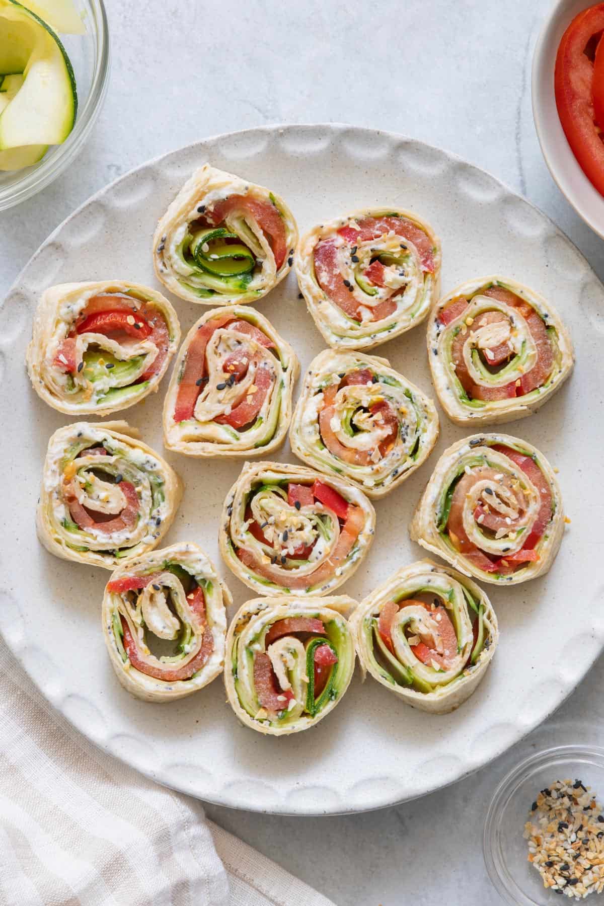 Everything bagel pinwheel sandwiches on a round plate with ingredients off screen on sides.