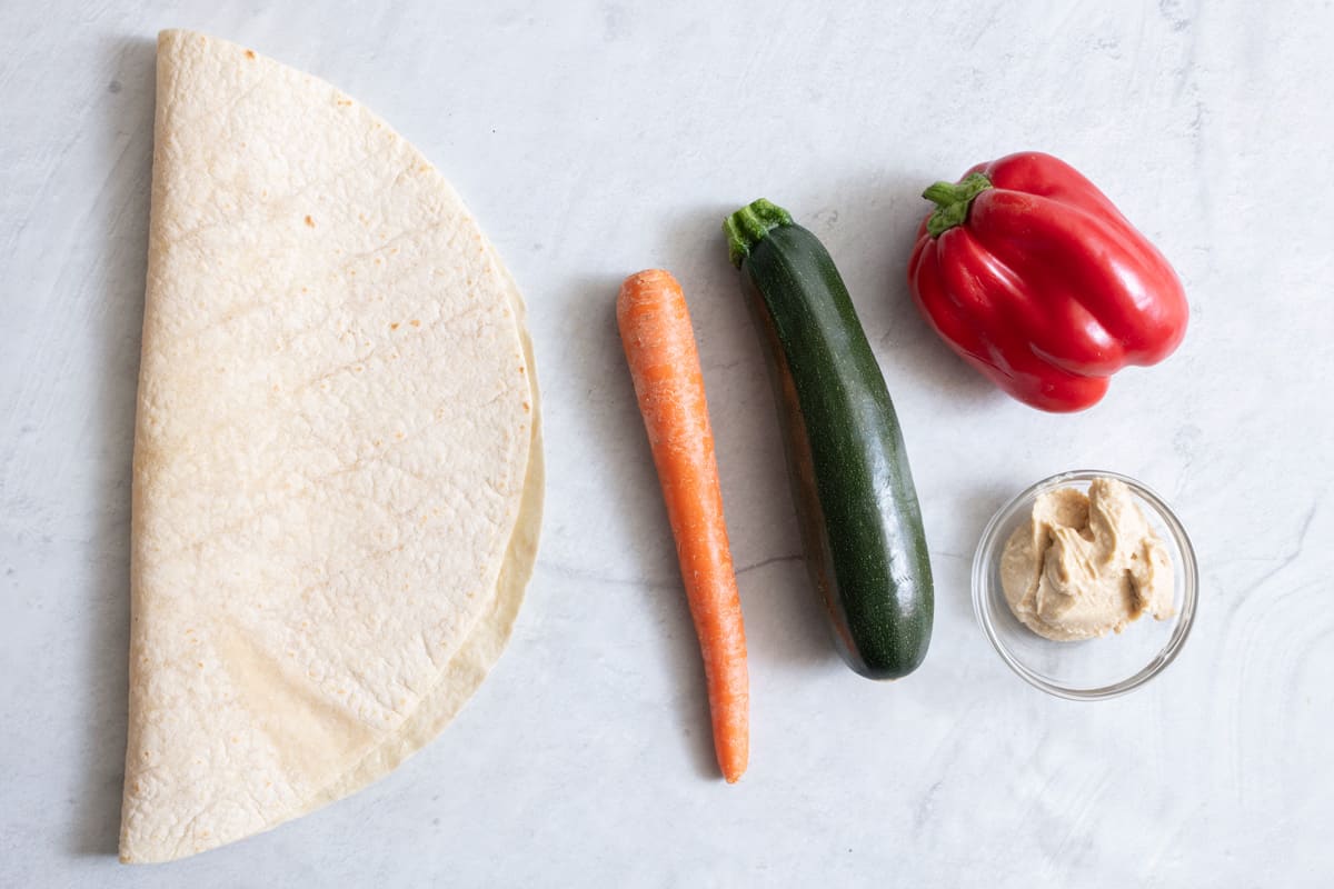 Ingredients for recipe: large tortilla shell, carrot, zucchini, red pepper, and hummus.