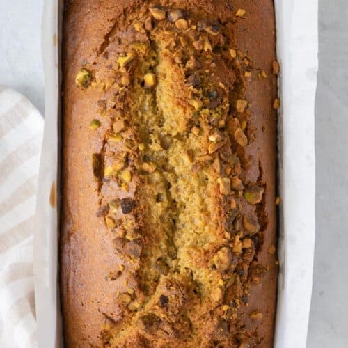 Pistachio bread loaf in pan with a folded napkin underneath.