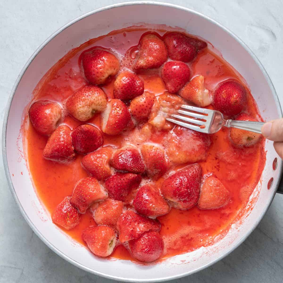 Fork smashing the berries in the pan.