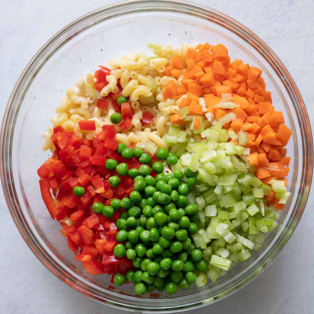 Macaroni added on top of dressing, celery, carrots, red pepper and peas on top.