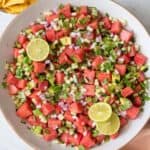 Large bowl of the watermelon salsa garnished with cilantro and lime slices with small bowl or tortilla chips to the side.