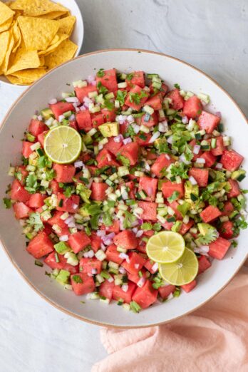 Large bowl of the watermelon salsa garnished with cilantro and lime slices with small bowl or tortilla chips to the side.