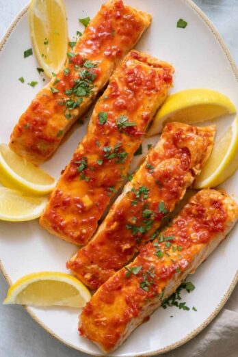 Large oval serving dish with 4 harissa glazed salmons filets garnished with lemon wedges and parsley.