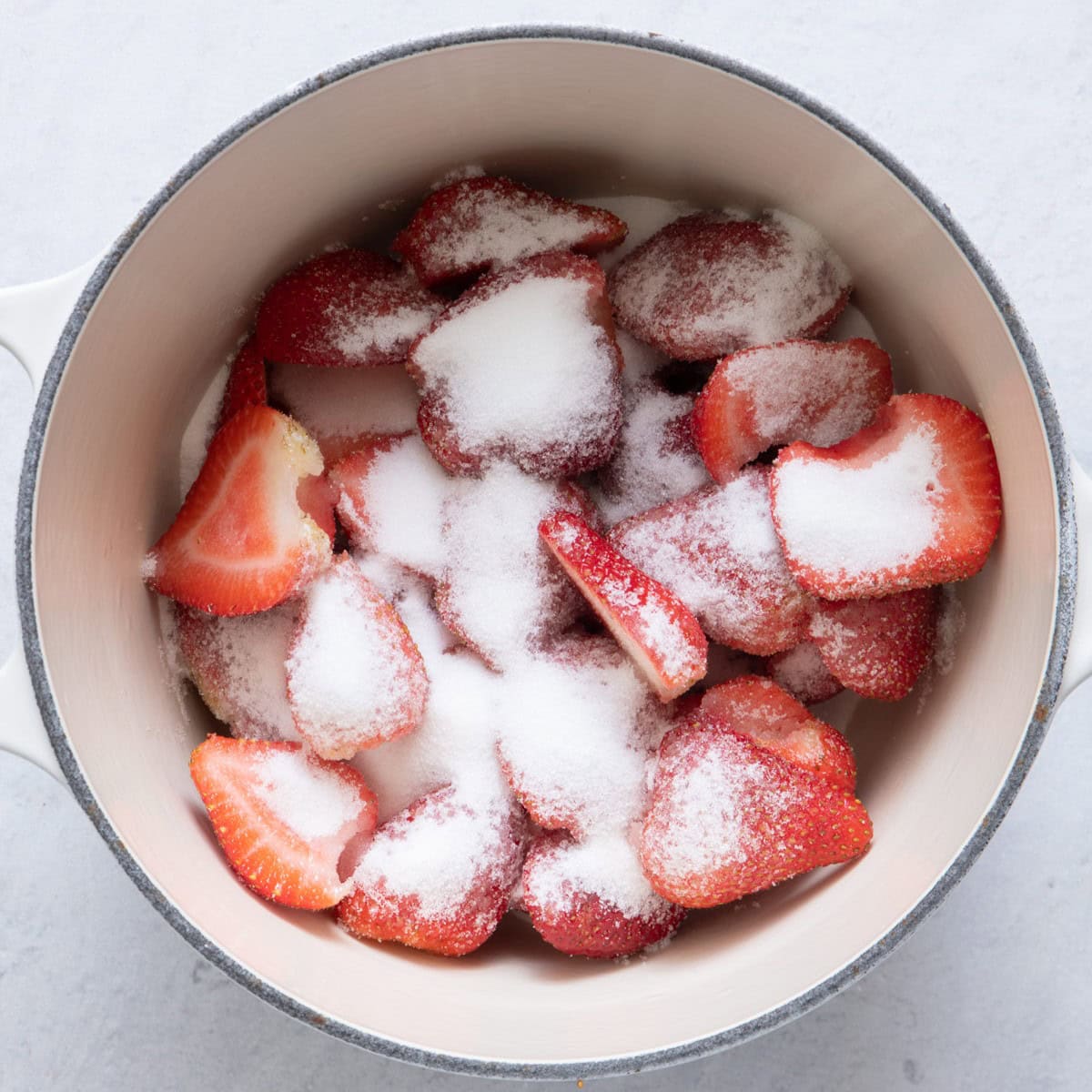 Sliced strawberries in saucepan with granulated sugar.