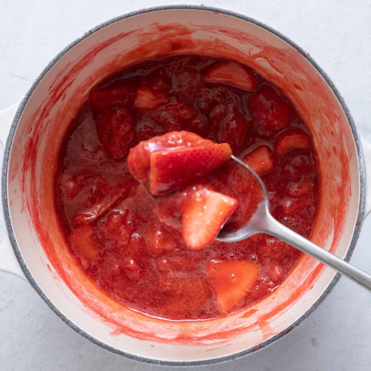 Spoon lifting up some of the thickened strawberry sauce.