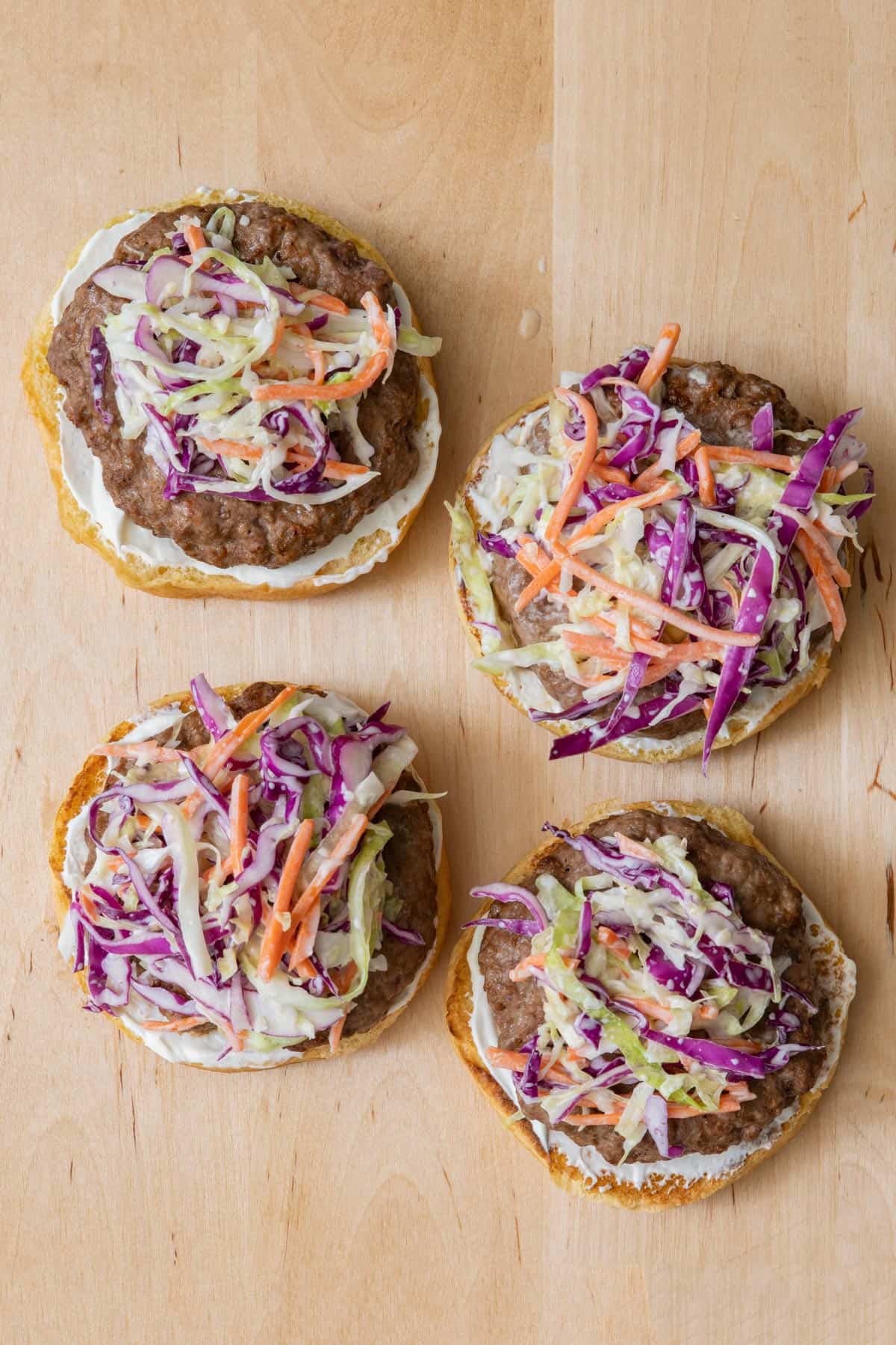 Top down view of four open faced burgers topped with coleslaw.