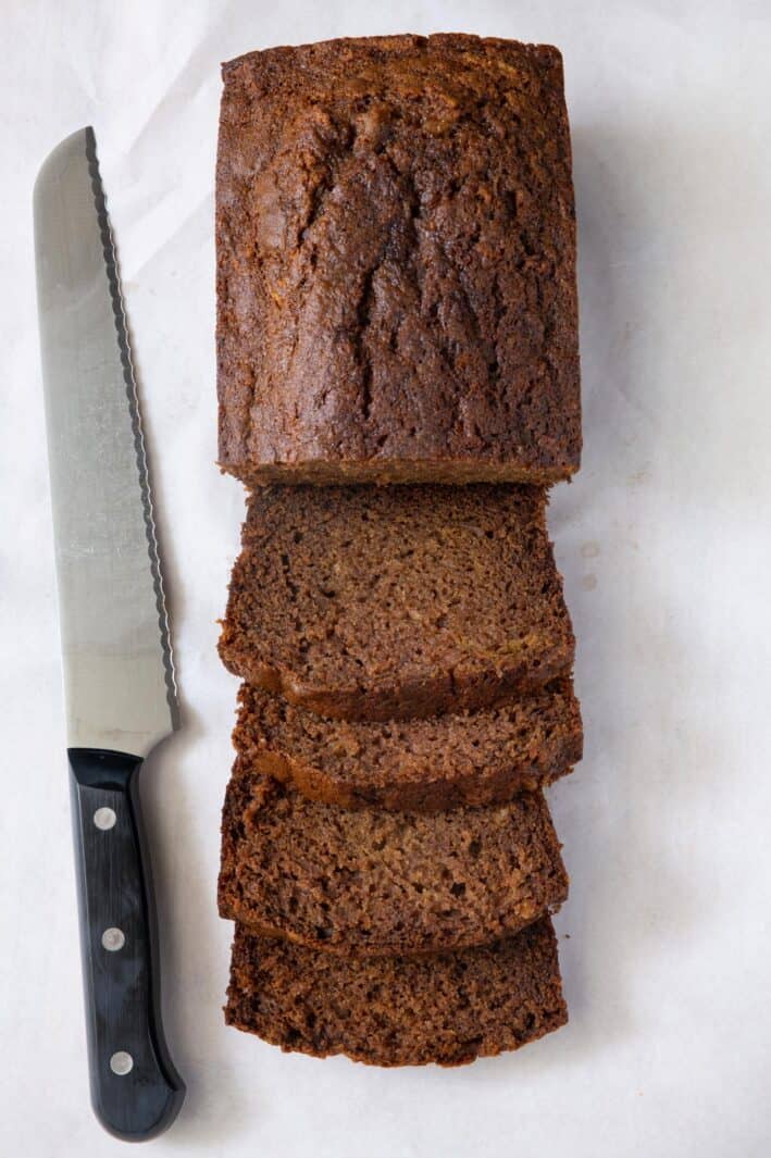 Half a loaf of Apple Bread sliced into thick pieces with remaining loaf uncut with a knife nearby.