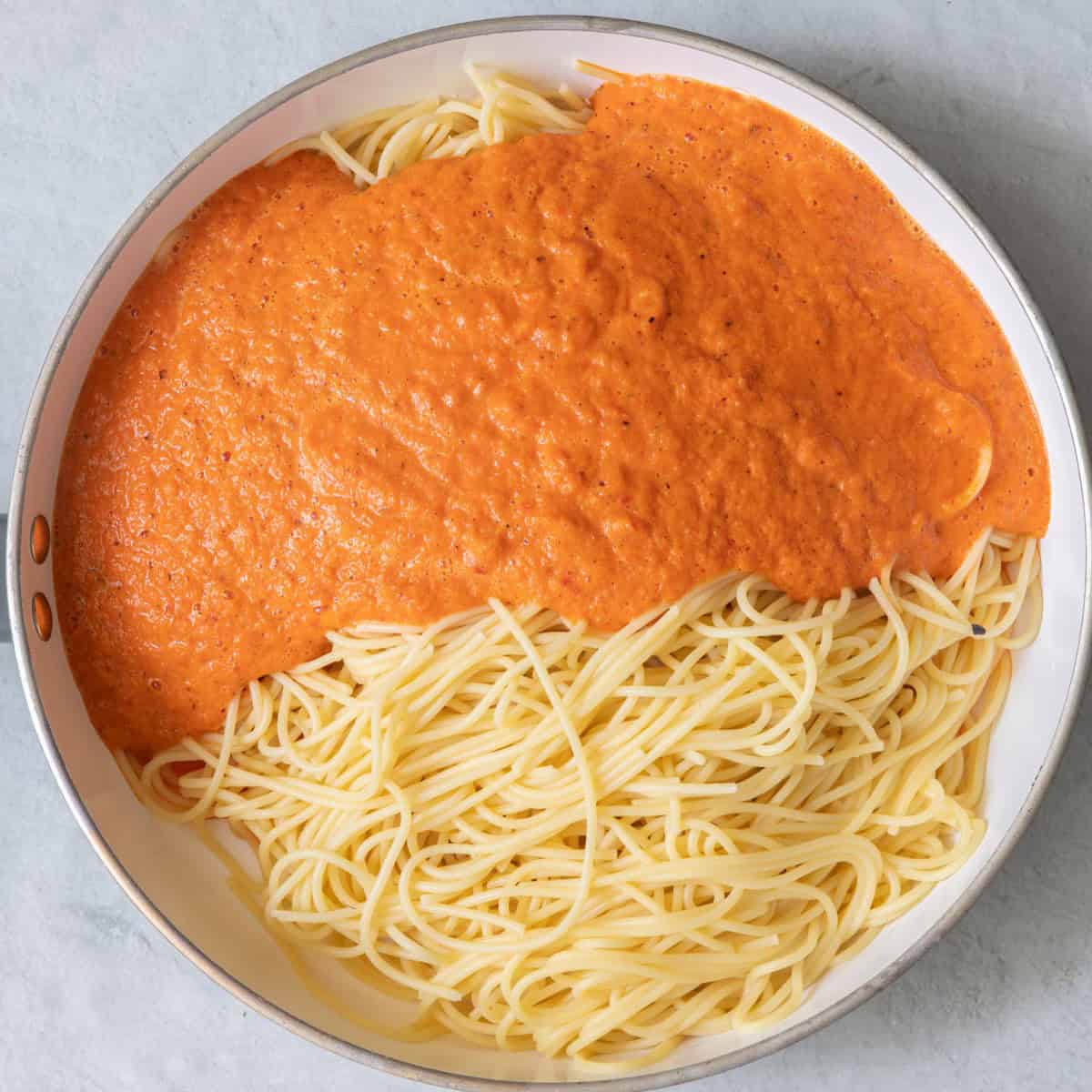 Sauce on top of cooked spaghetti in skillet.