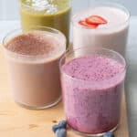 4 different smoothie recipes in short glasses sitting on wood board.
