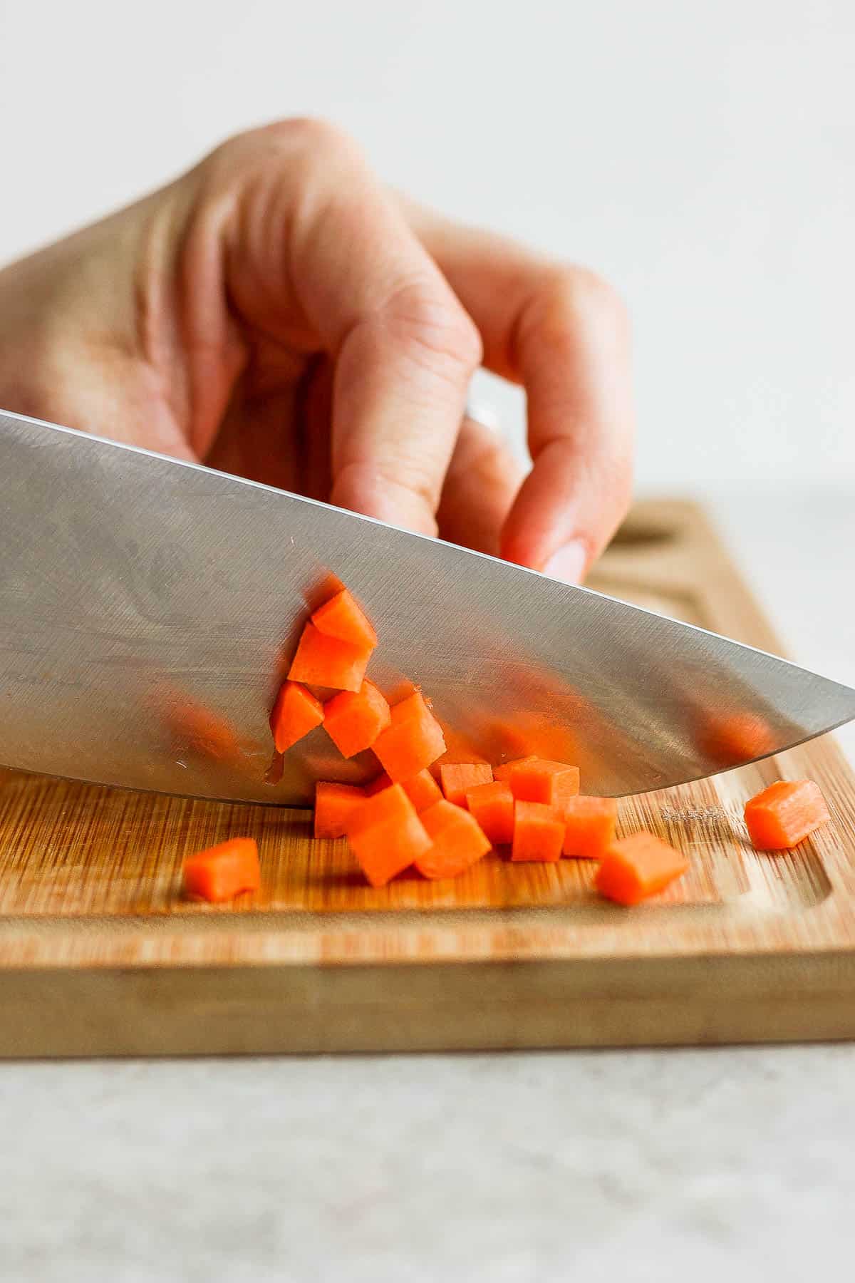 Carrot being diced on a cutting board with a large knife.