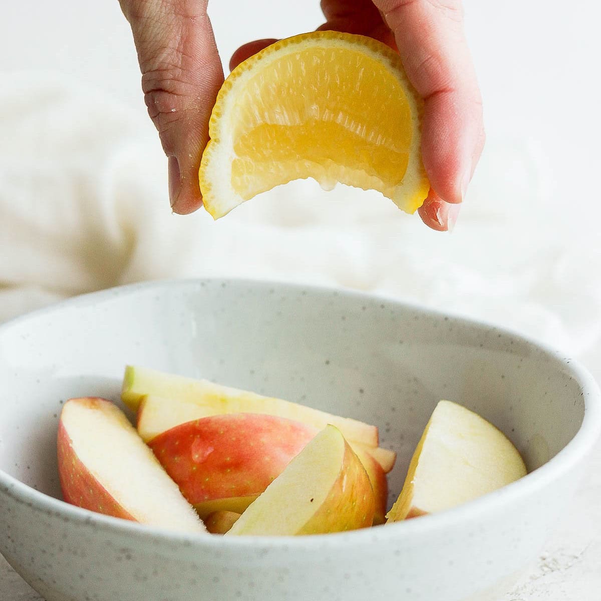 Apples in tupperware with half lemon getting squeezed on top.