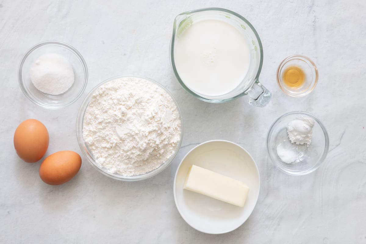 Ingredients for recipe in individual dishes: flour, sugar, baking powder, salt, 2 eggs, milk, vanilla, and part of a stick of butter.