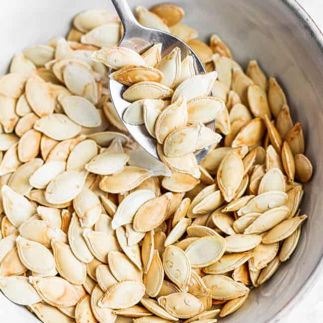 Small bowl of roasted pumpkin seeds with spoon scooping some.