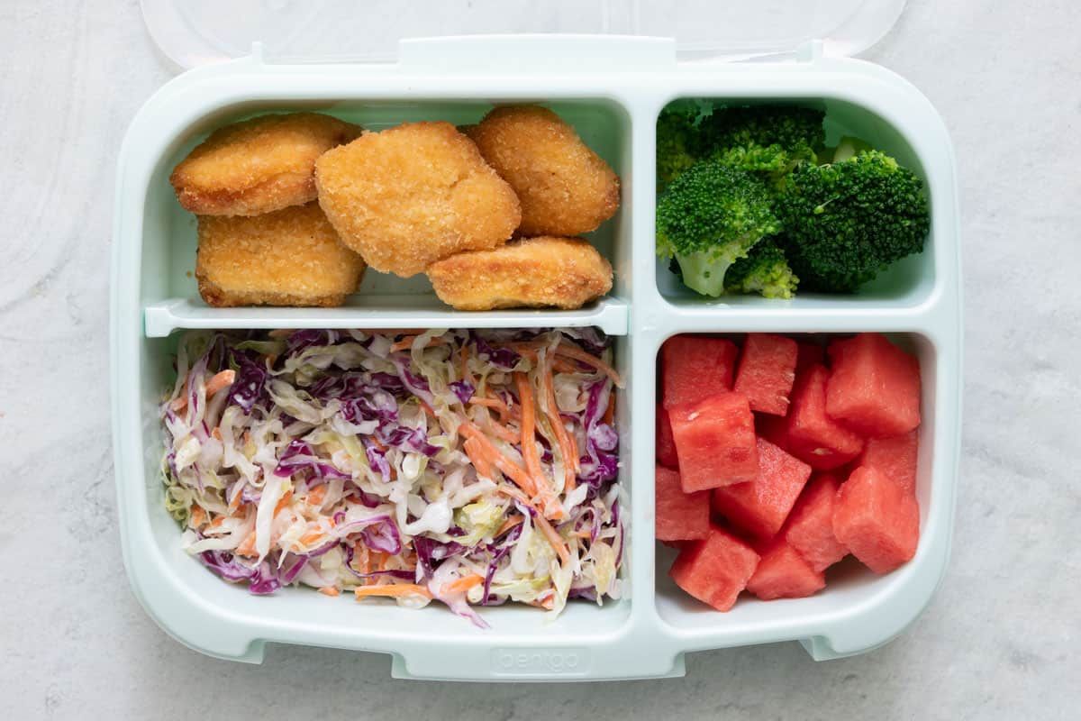 Lunchbox with 4 sections with different foods in each section: chicken nuggets, coleslaw, broccoli, and watermelon cubes.