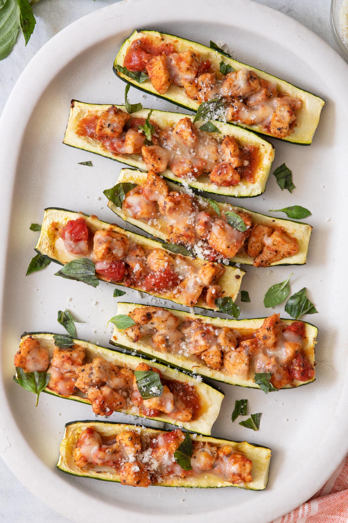 Large oval serving plate with zucchini boats stuffed with chicken and topped with cheese.
