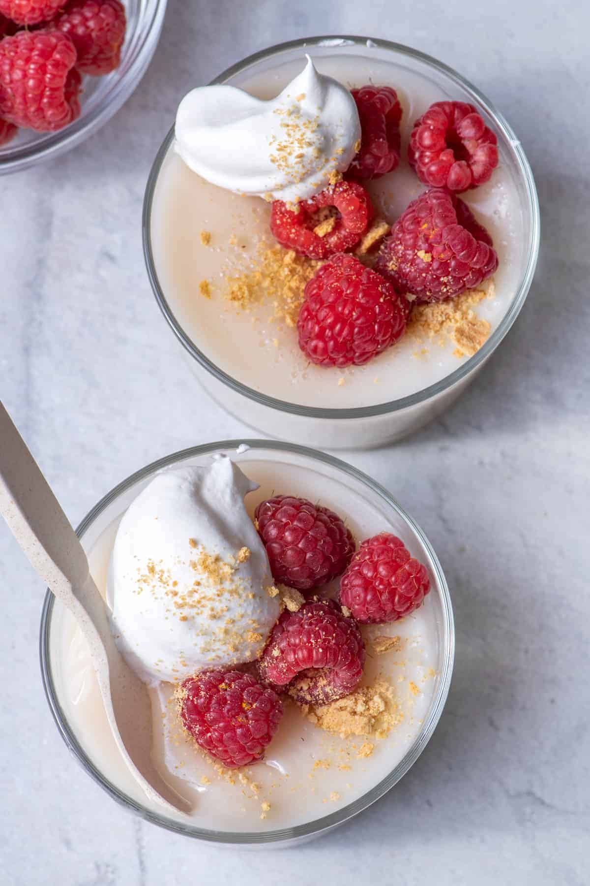 Homemade vegan pudding topped with berries and cream - top down view of the two glass jars
