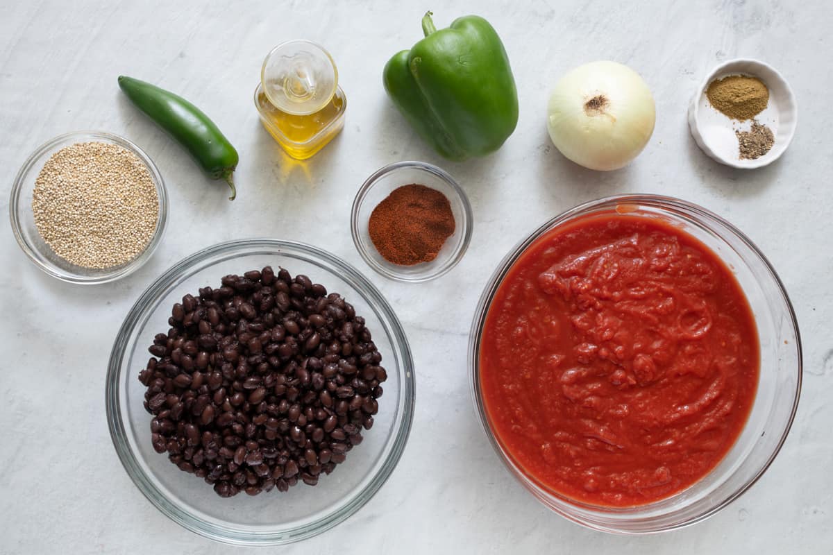 Ingredients for recipe before prepping: uncooked quinoa, jalapeno, black beans, oil, chili powder, green bell pepper, onion, crushed tomatoes, and spices.