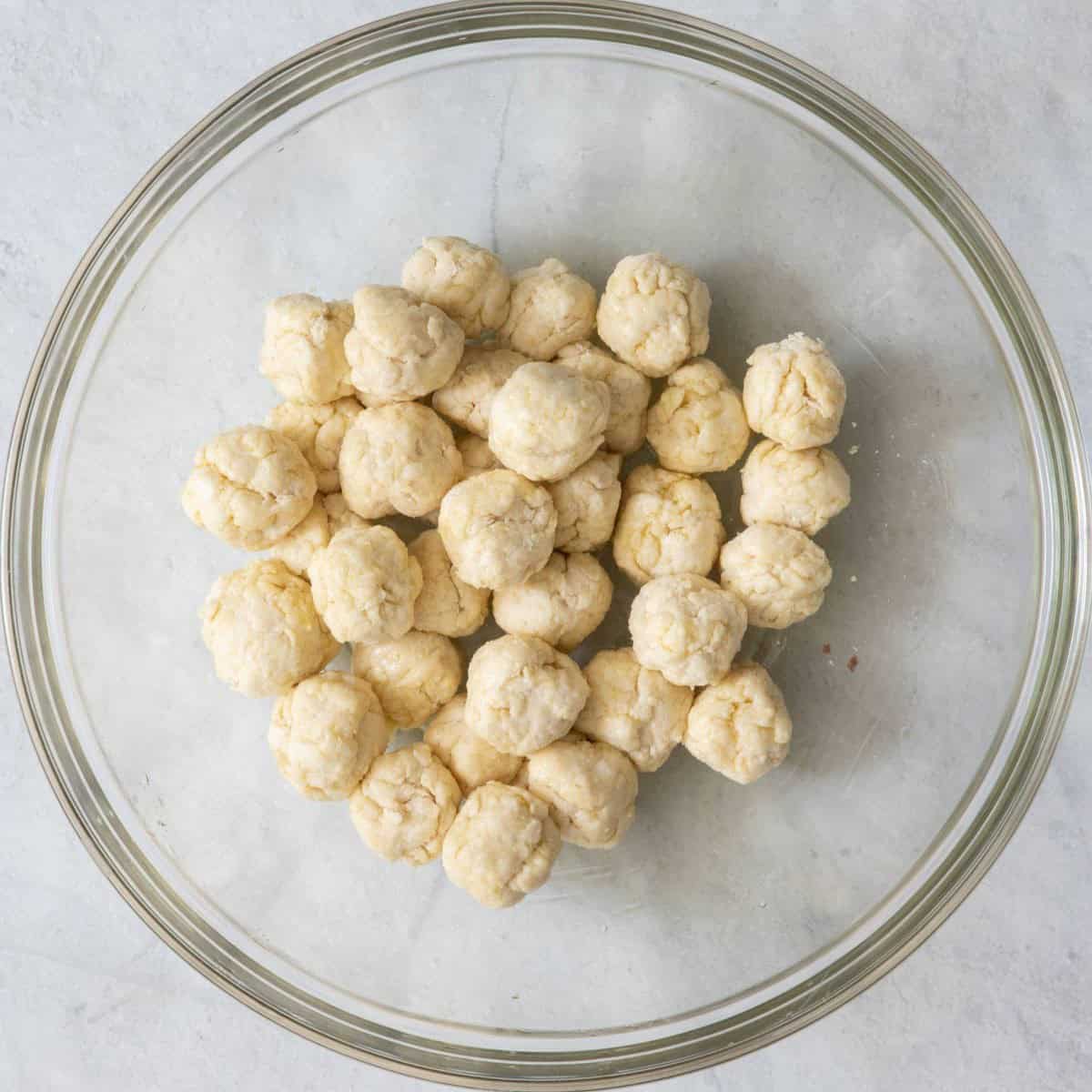 Adding the dough balls into a bowl and covering them with olive oil.
