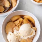 Small bowl of baked apple slices with ice cream scooped on top and extra apples to the side.