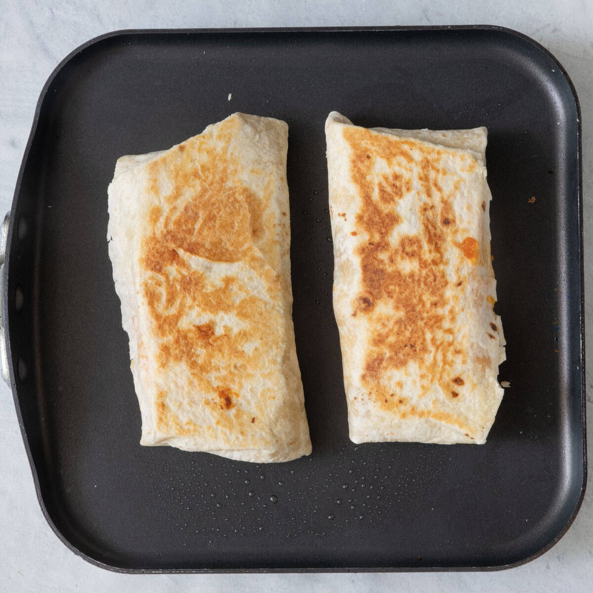 2 burritos on pan after flipped showing golden brown on seam.
