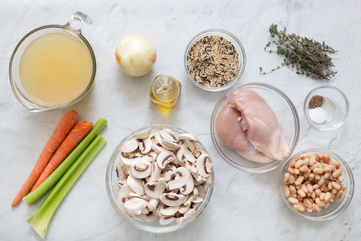 Ingredients before being prepped: broth, carrots, celery, onion, oil, sliced mushrooms, wild rice, chicken, beans, fresh thyme, and seasoning.