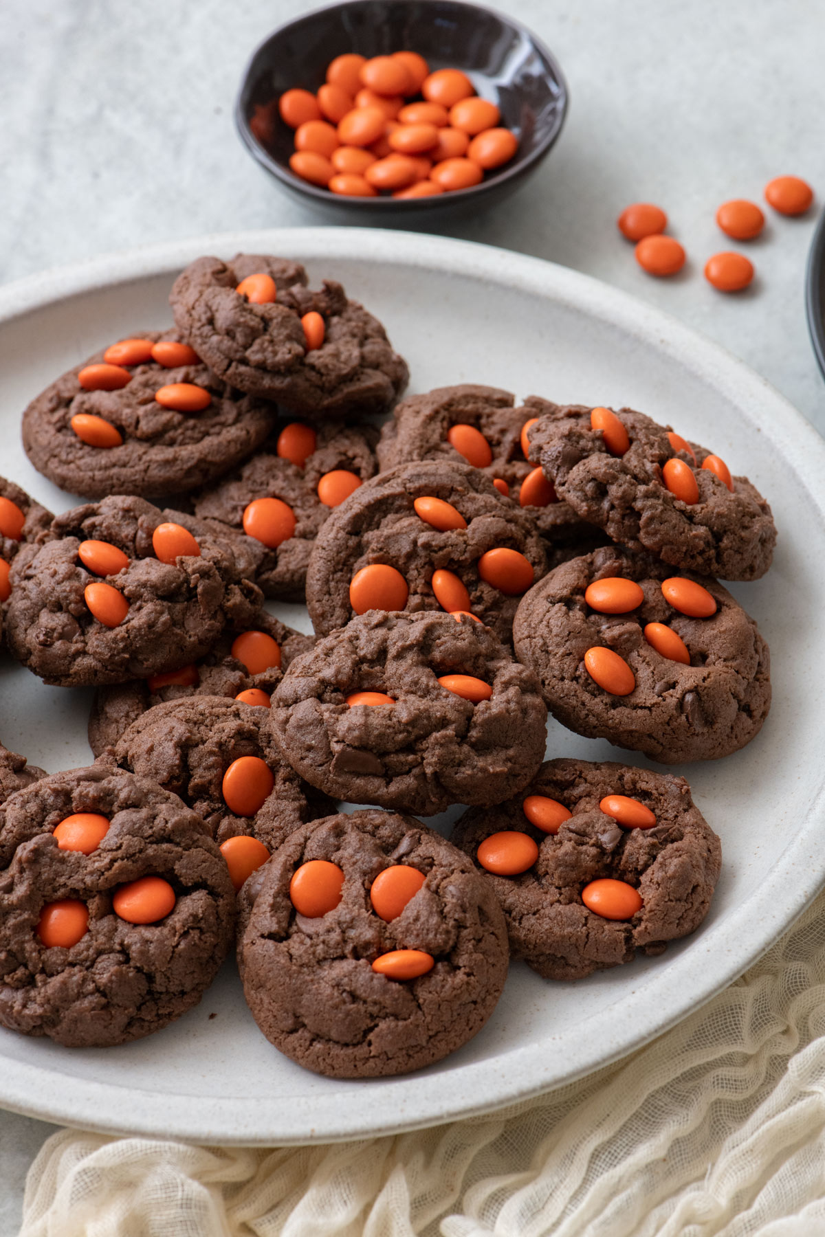 Large white plate with dark chocolate cookies with orange candies and small pumpkins nearby.