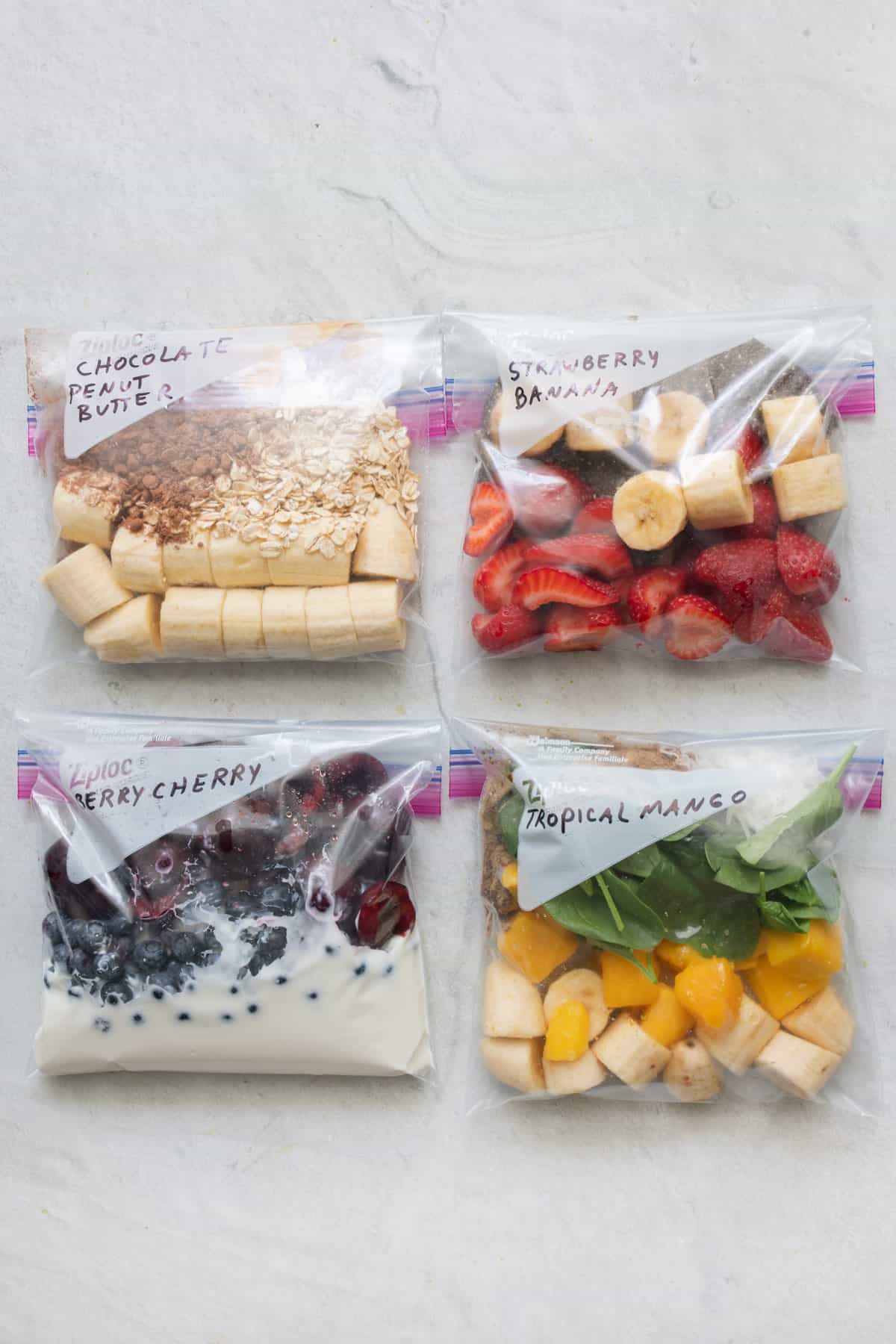 four ziptop bags with smoothie ingredients inside ready to go in the freezer to make smoothie packs.