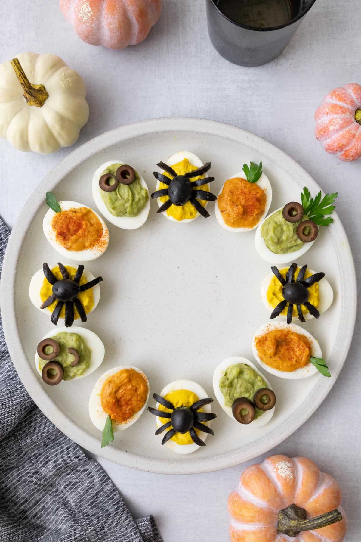 3 different halloween inspired devilled eggs place around the edge of a large plate with mini pumpkin decorated around.