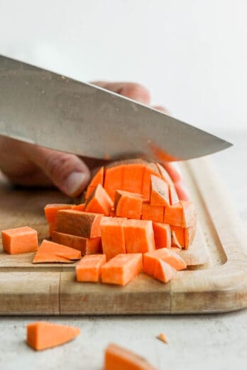 Cutting sweet potatoes on a cutting board into cubes.