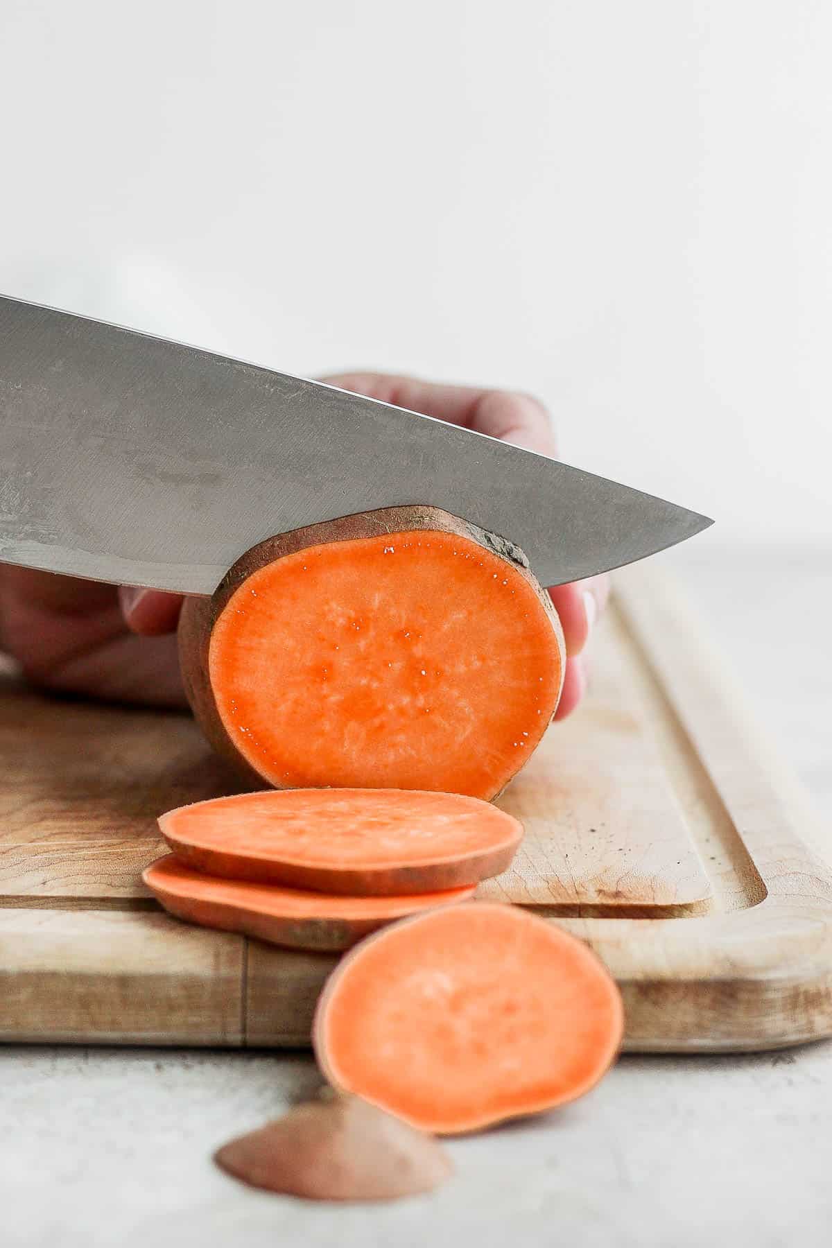 Close up of sweet potato being sliced in rounds.