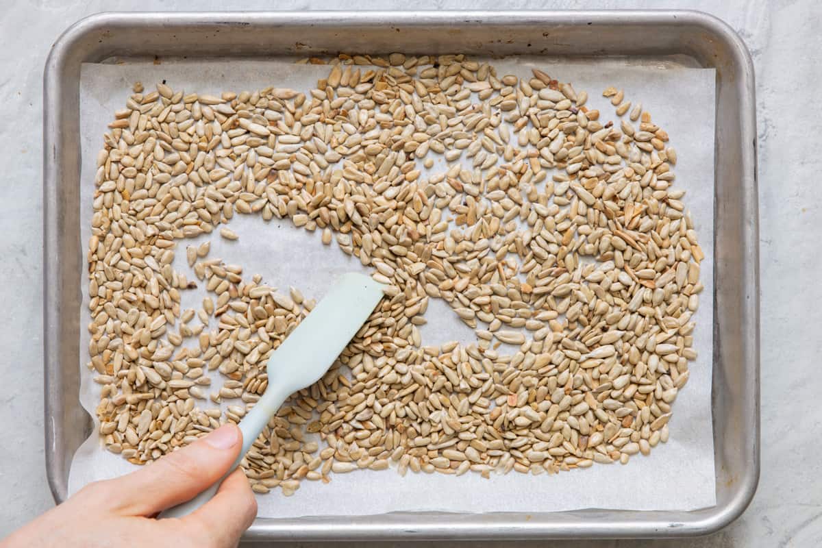 Roasted seeds on baking sheet lined with parchment paper with spatula moving some.