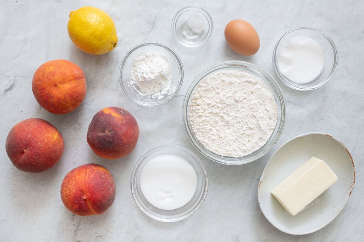 Ingredients for recipe: four whole peaches, 1 lemon, sugar, corn starch, salt, flour, egg, and stick of butter.
