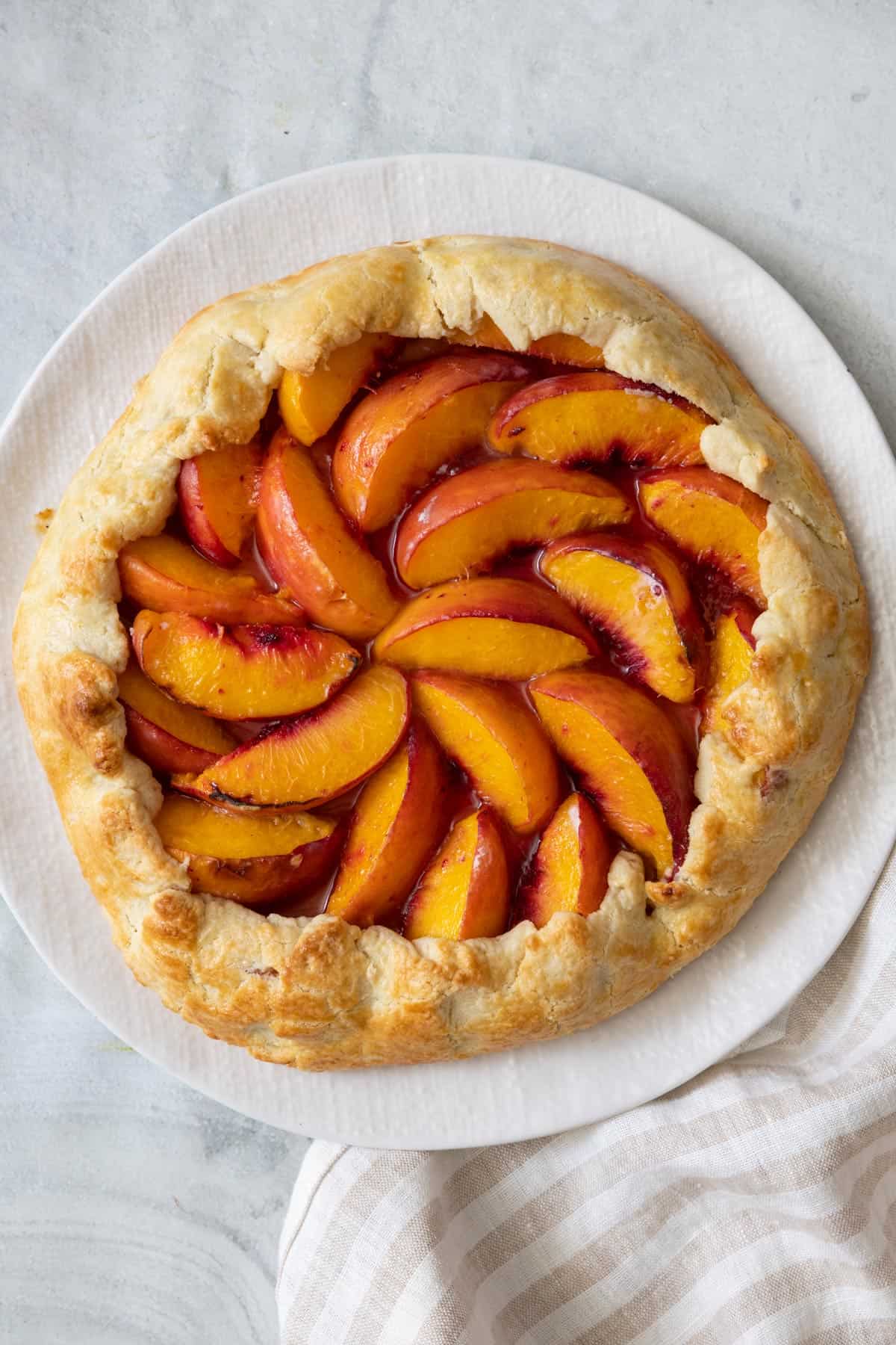 Peach galette on a white round plate after baking.