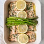 Roasted salmon and asparagus in baking dish garnished with thin lemon slices.