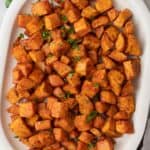 Diced roasted sweet potatoes on large white oval serving dish garnished with fresh parsley.