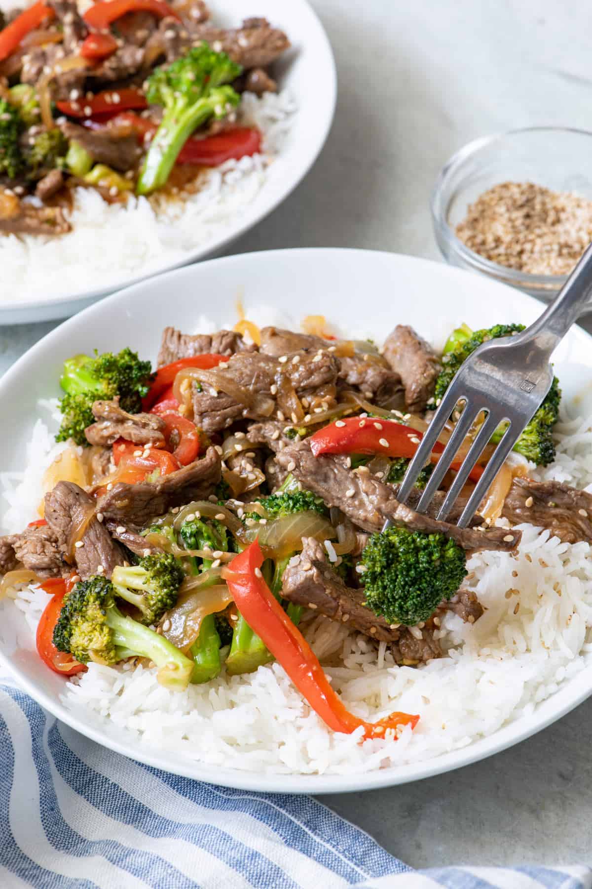 Close up of teriyaki beef stir fry served over white rice with a fork picking up a bite.