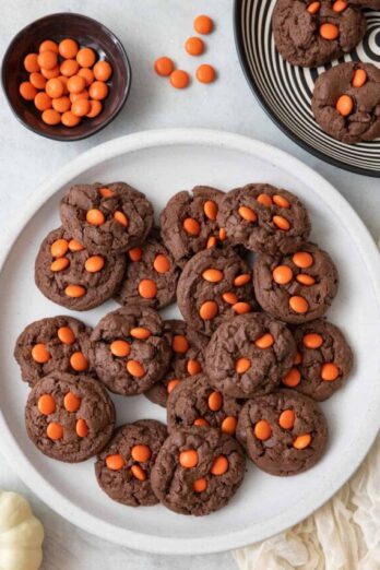 Plate of cookies on large white plate with orange candies nearby and a black and white swirl plate with a few cookies on it.