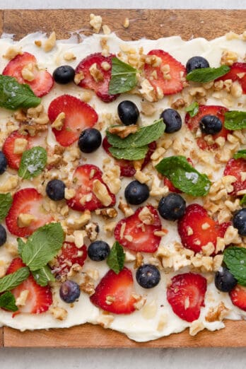 Butter board topped with sliced strawberries, blueberries, nuts, and fresh mint leaves.